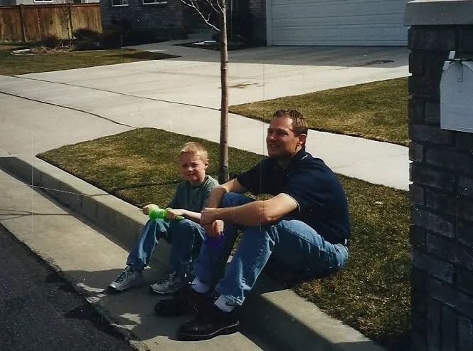 Jeremy as a boy, sitting on a curb beside his dad.