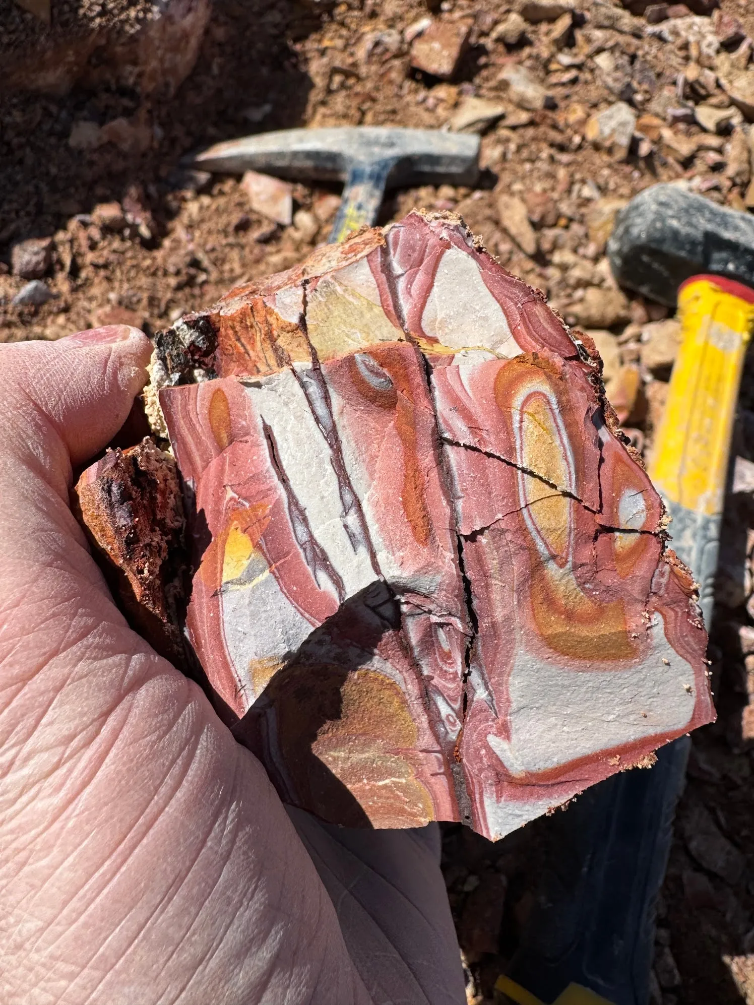 A freshly broken rock banded pink, white, and orange, next to a rock hammer.